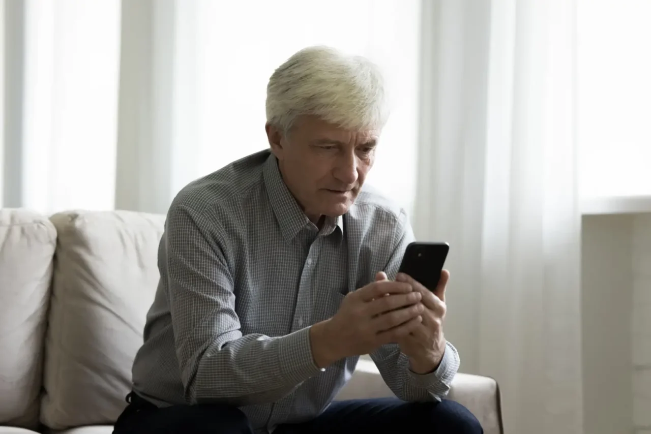 Starší muž si v telefonu čte zprávu o důchodech a reaguje na ni s rozpaky.