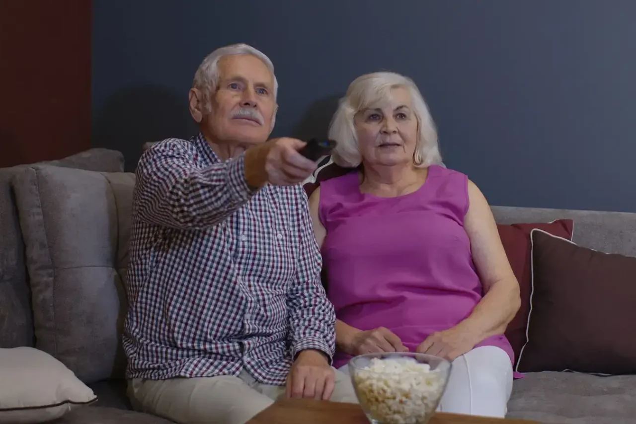 Manželé v důchodu sledují televizi a čekají na konec poplatků.
