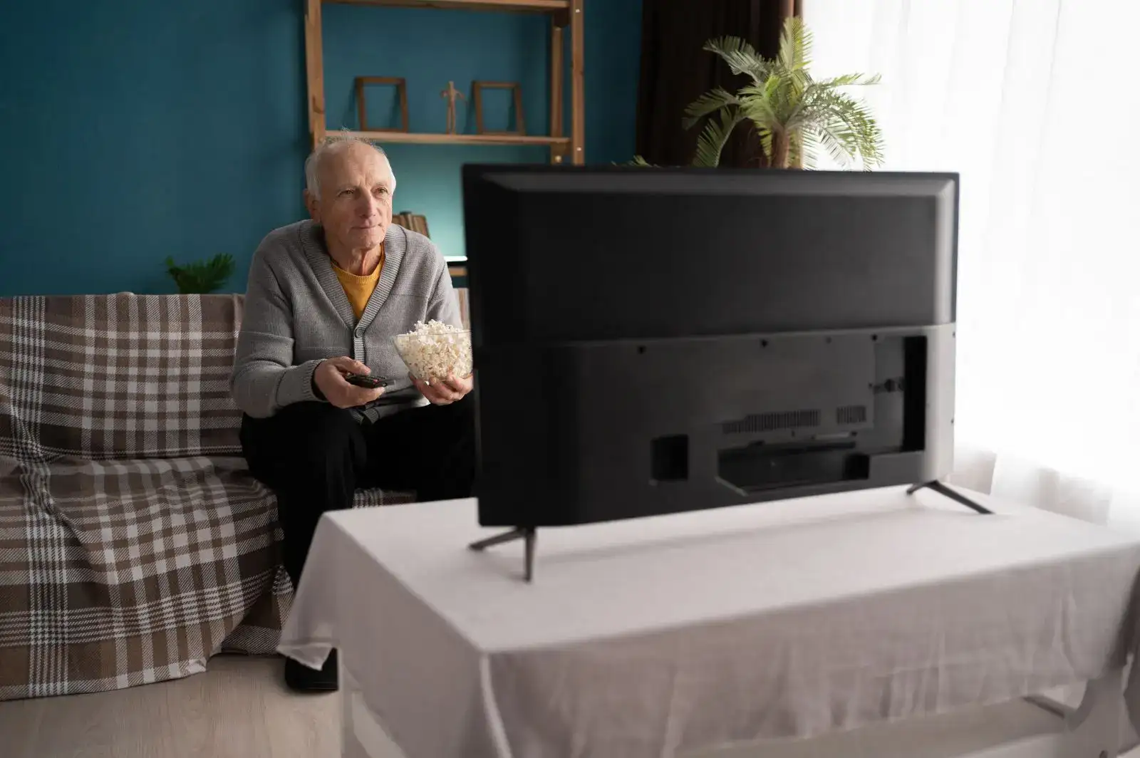 Senior sleduje doma televizi.