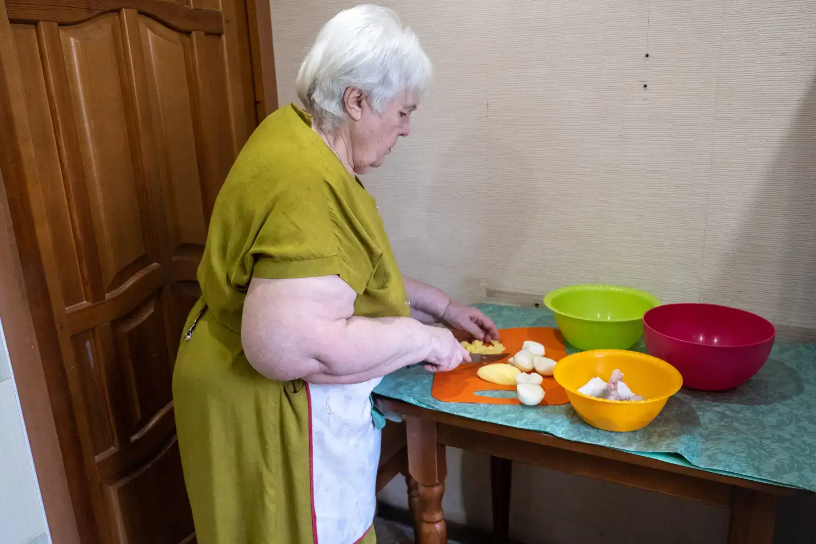 Seniorka chystá brambory do polévky.