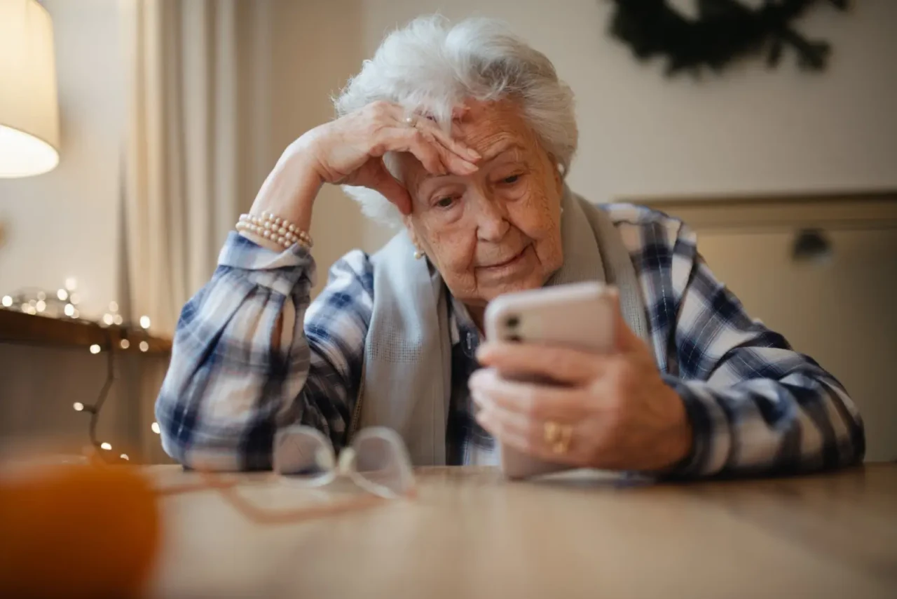 Seniorka si v mobilu ověřuje informace a snaží se pochopit pravidla kolem zrušení poplatků pro důchodce.