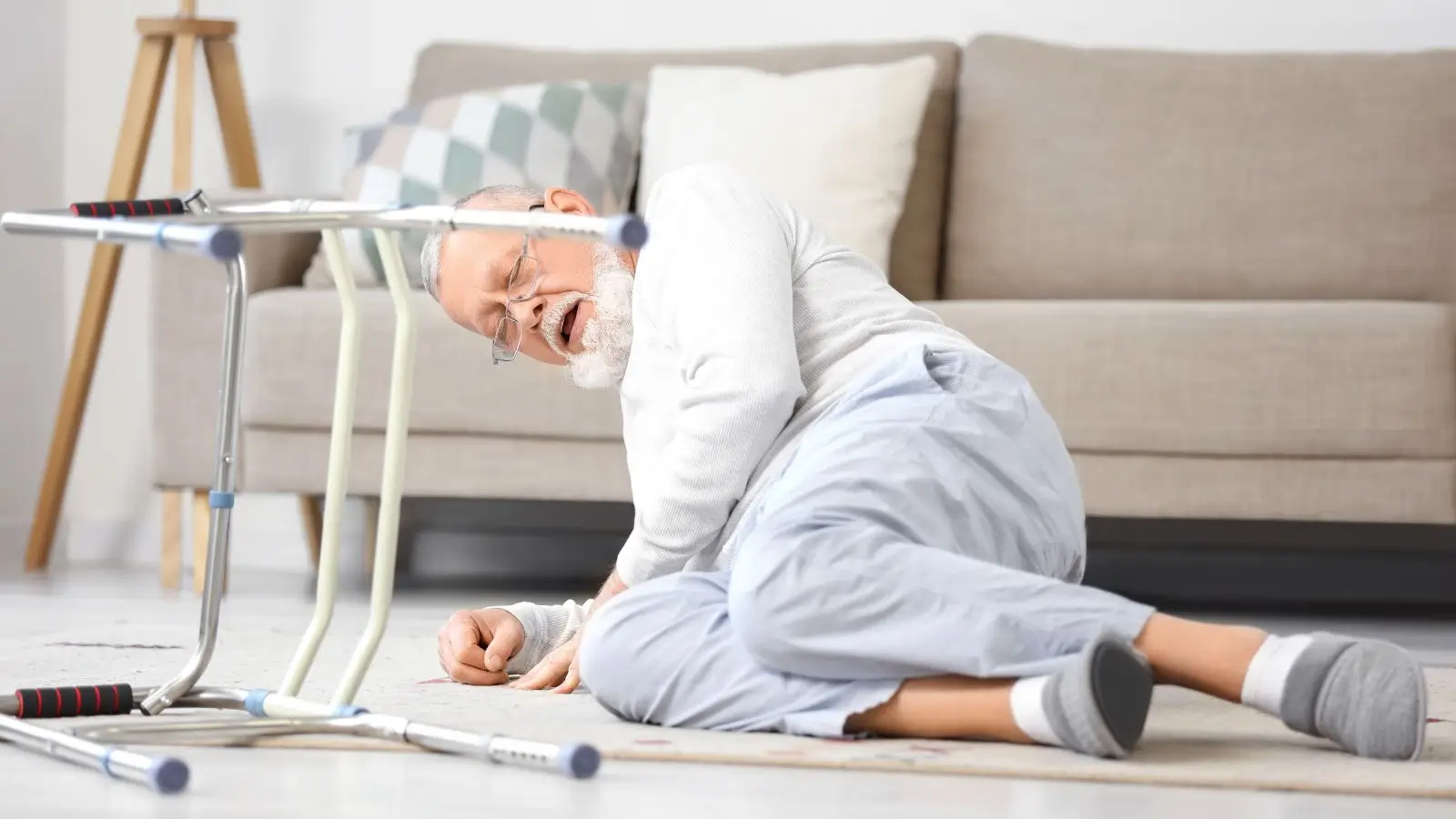 Senior leží po pádu na podlaze v obývacím pokoji. Pády v domácnosti mohou mít u starších lidí vážné zdravotní následky.