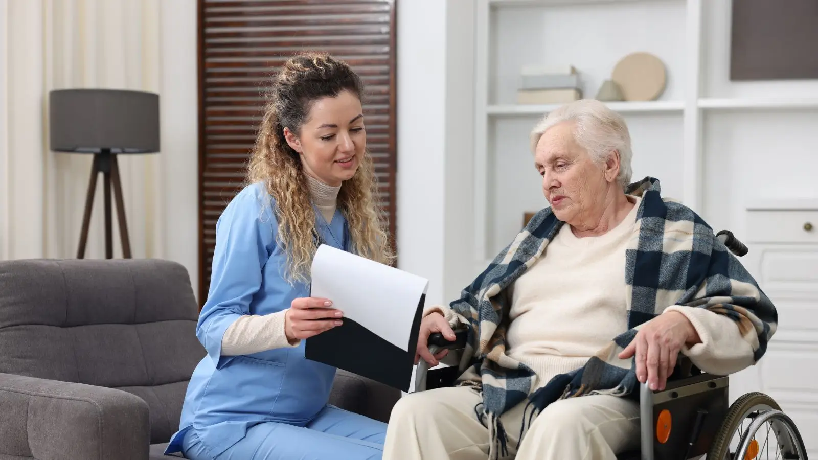 Seniorka na invalidním vozíku konzultuje s pečovatelkou dokumenty.