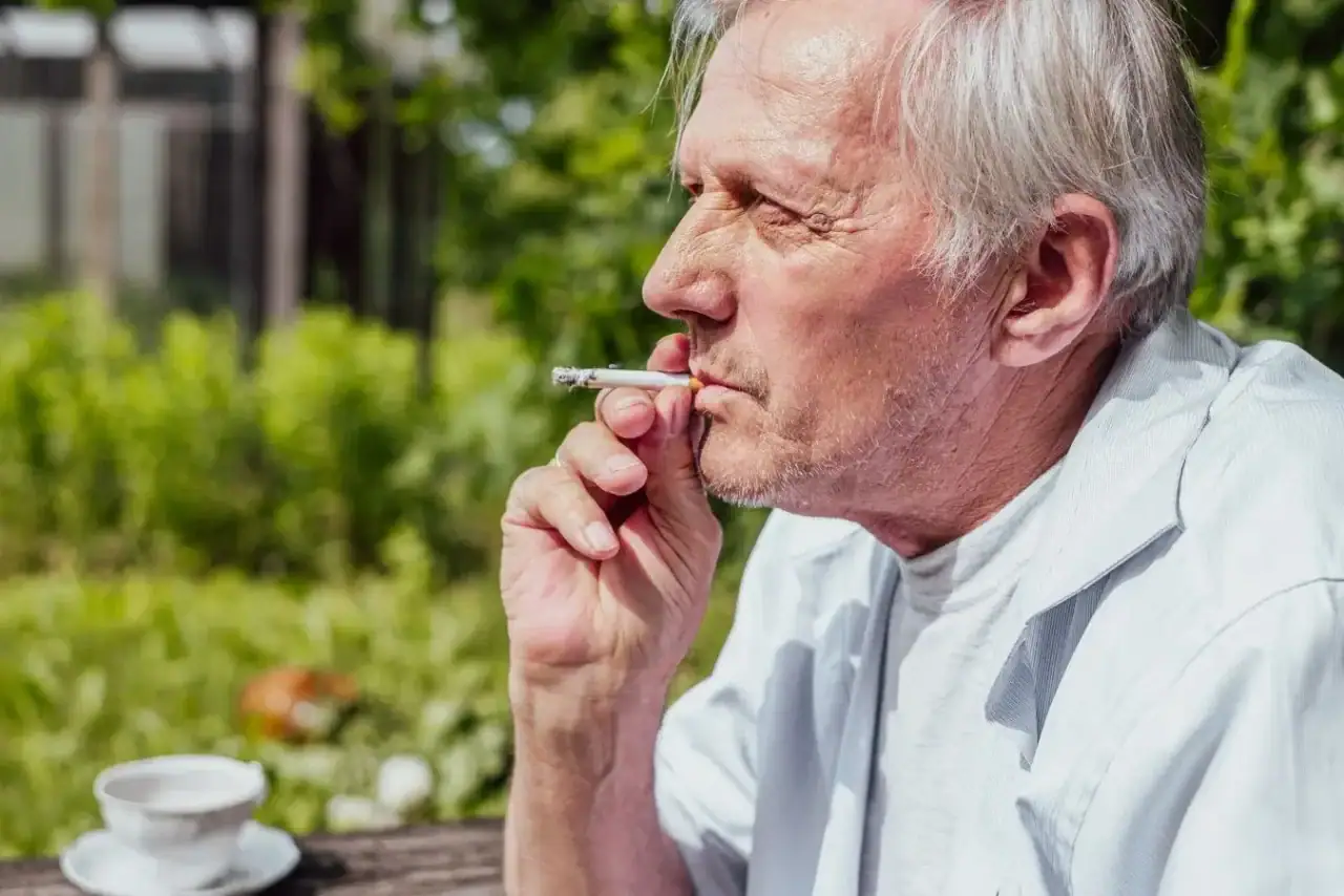 Senior kouří cigaretu u kávy.