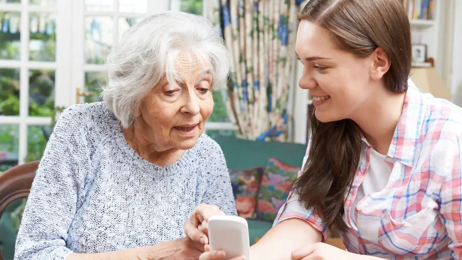 Mladá žena radí seniorce s mobilním telefonem,