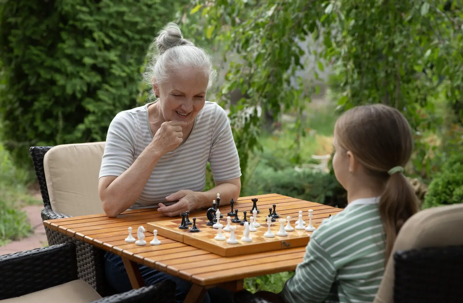 Seniorka tráví s vnučkou čas nad partií šachů.